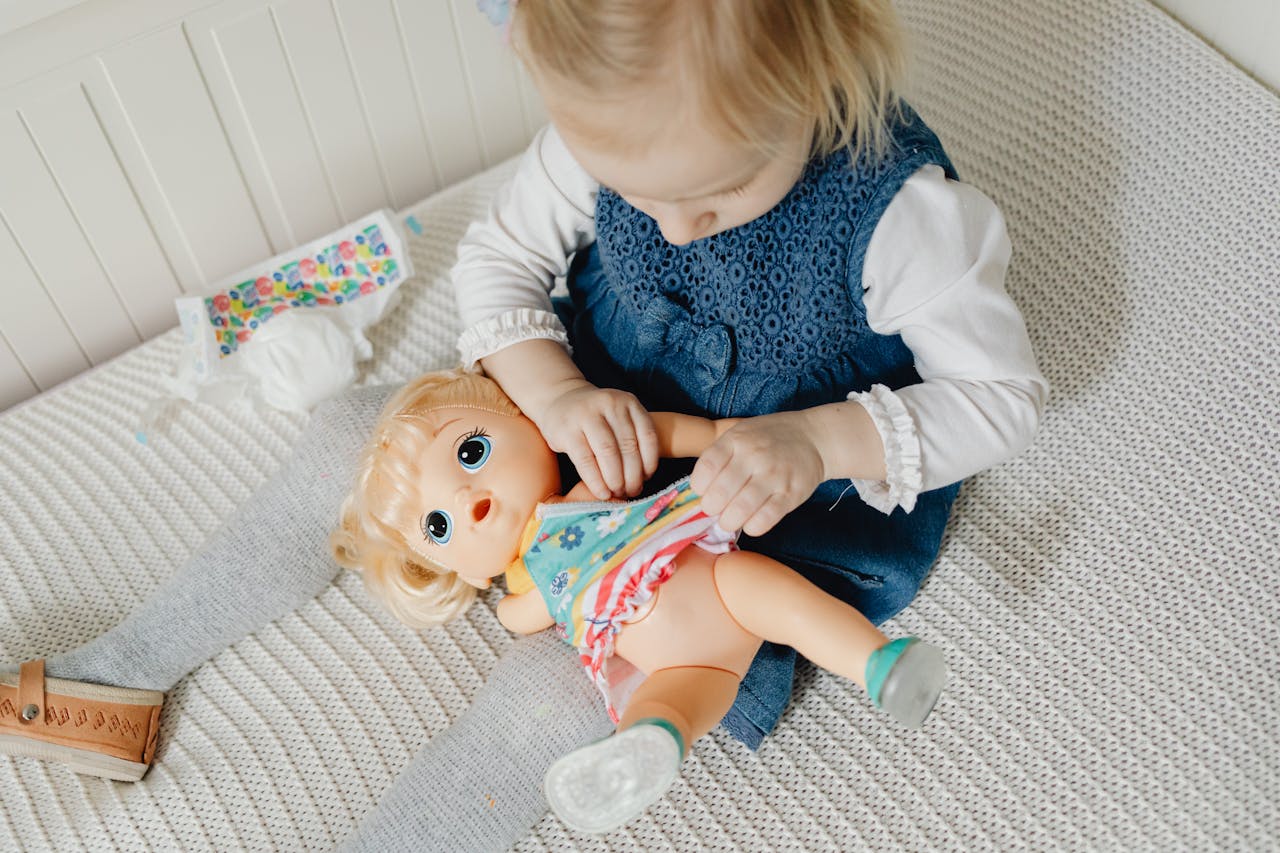 A little girl happily dresses her doll in a cozy indoor setting, capturing playful childhood moments.